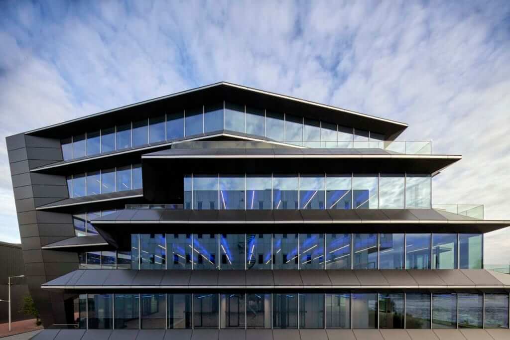 A futuristic multi-story office building with large glass windows and a sleek black facade, reflecting the sky in the daytime.