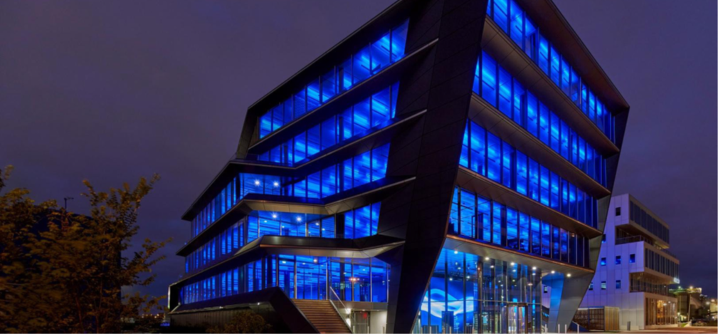 A modern, angular office building illuminated with striking blue LED lights at night, showcasing innovative architectural design.