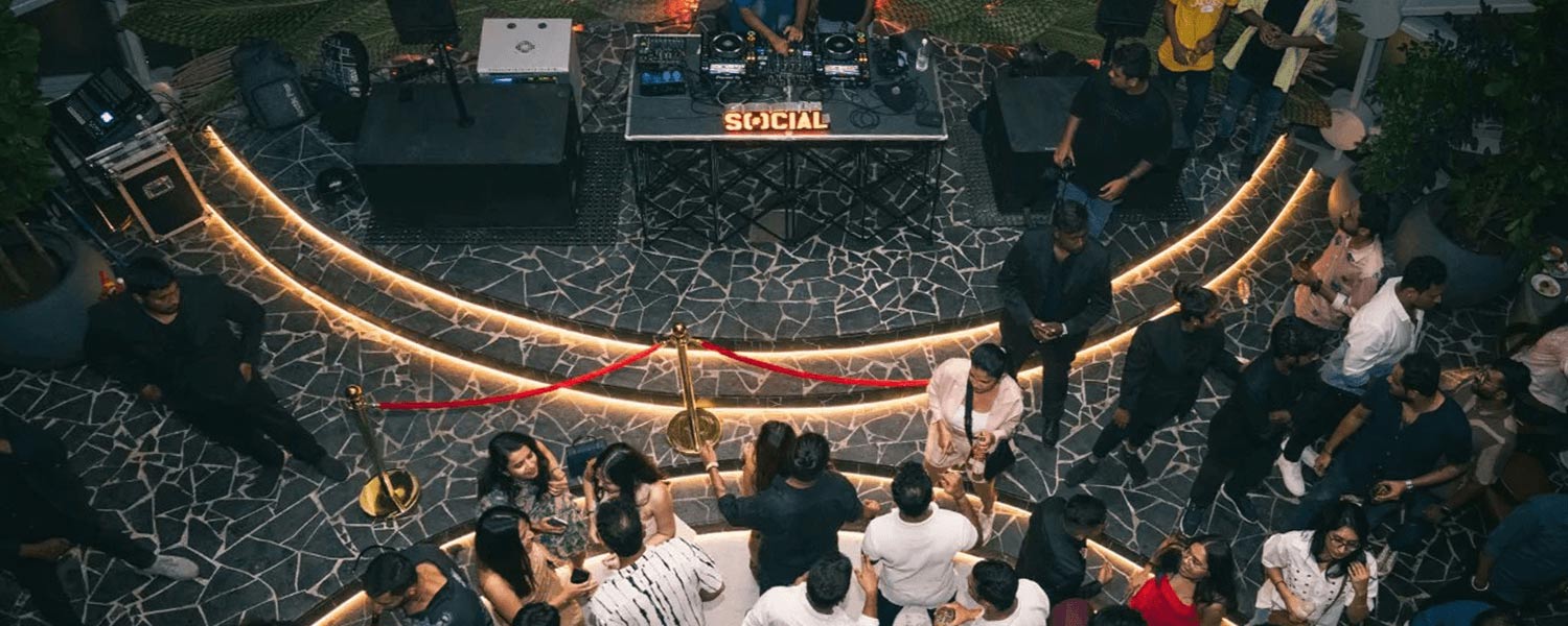 A vibrant nightlife scene at Bellandur SOCIAL, featuring a DJ setup with Powersoft amplifiers and a lively crowd enjoying immersive sound.